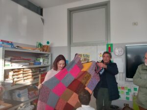 Coperta di lana formata da quadrati di colori diversi tenuta da due maestre